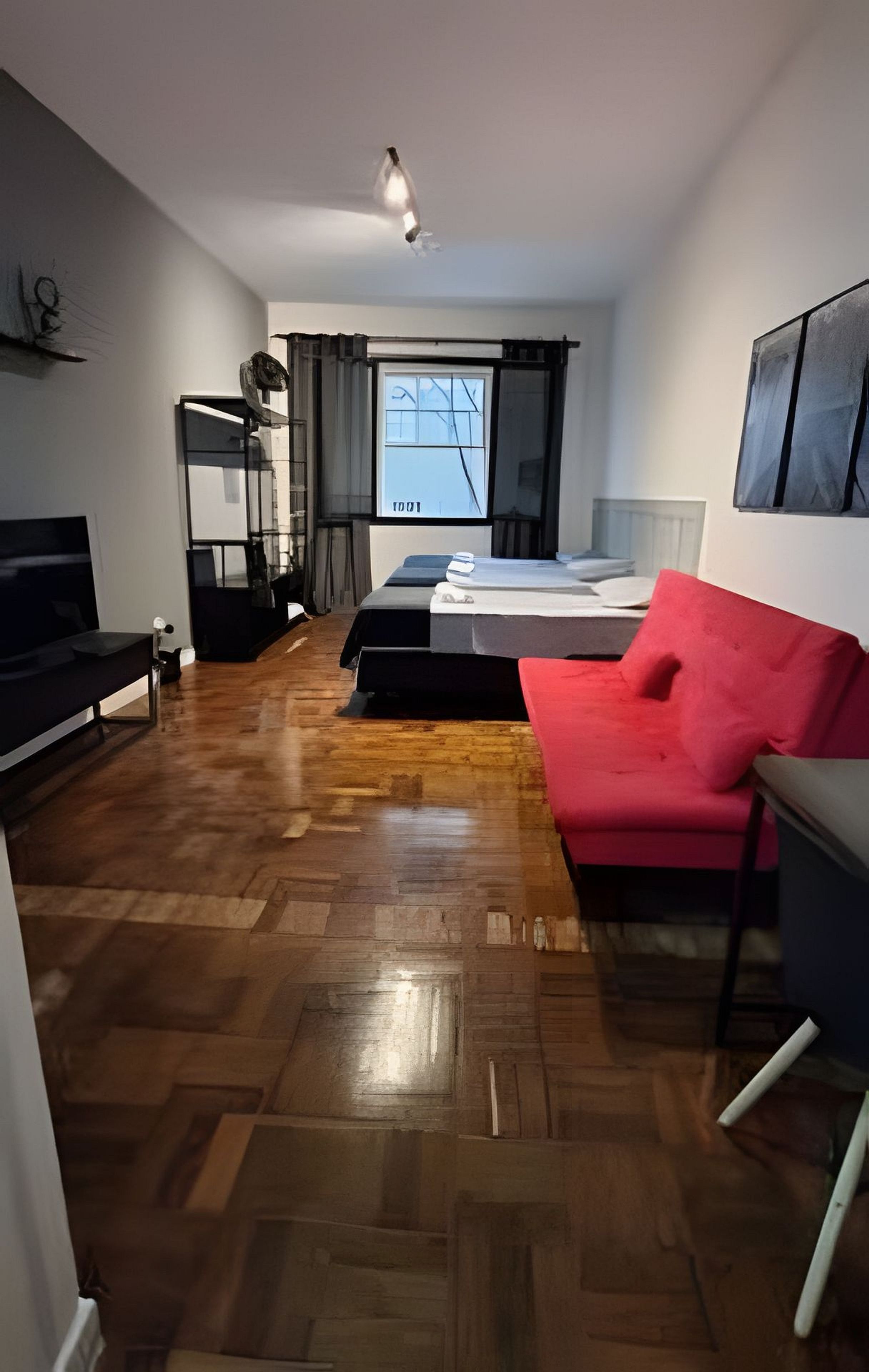 Uma sala de estar moderna com uma cama, um sofá vermelho e uma televisão.