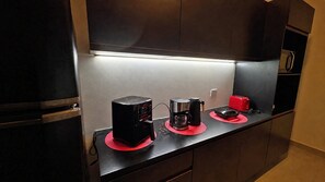 Una encimera de cocina con cafetera, tostadora y un electrodoméstico rojo, posiblemente una cocedora de arroz o de cocción lenta, sobre tapetes rojos.