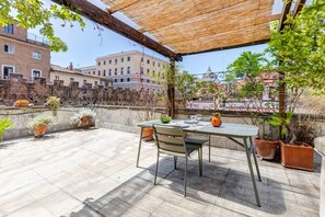 A rooftop terrace with a table and chairs, potted plants, and a view of buildings. - Vatican Amazing Terrace St Peter (Roma)