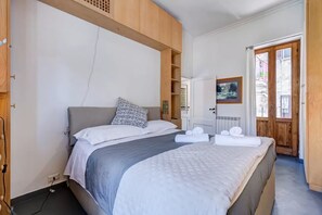Ein Schlafzimmer mit einem Bett, einem Holzkopfstück, einer weißen Wand, einer Tür und einem Fenster.