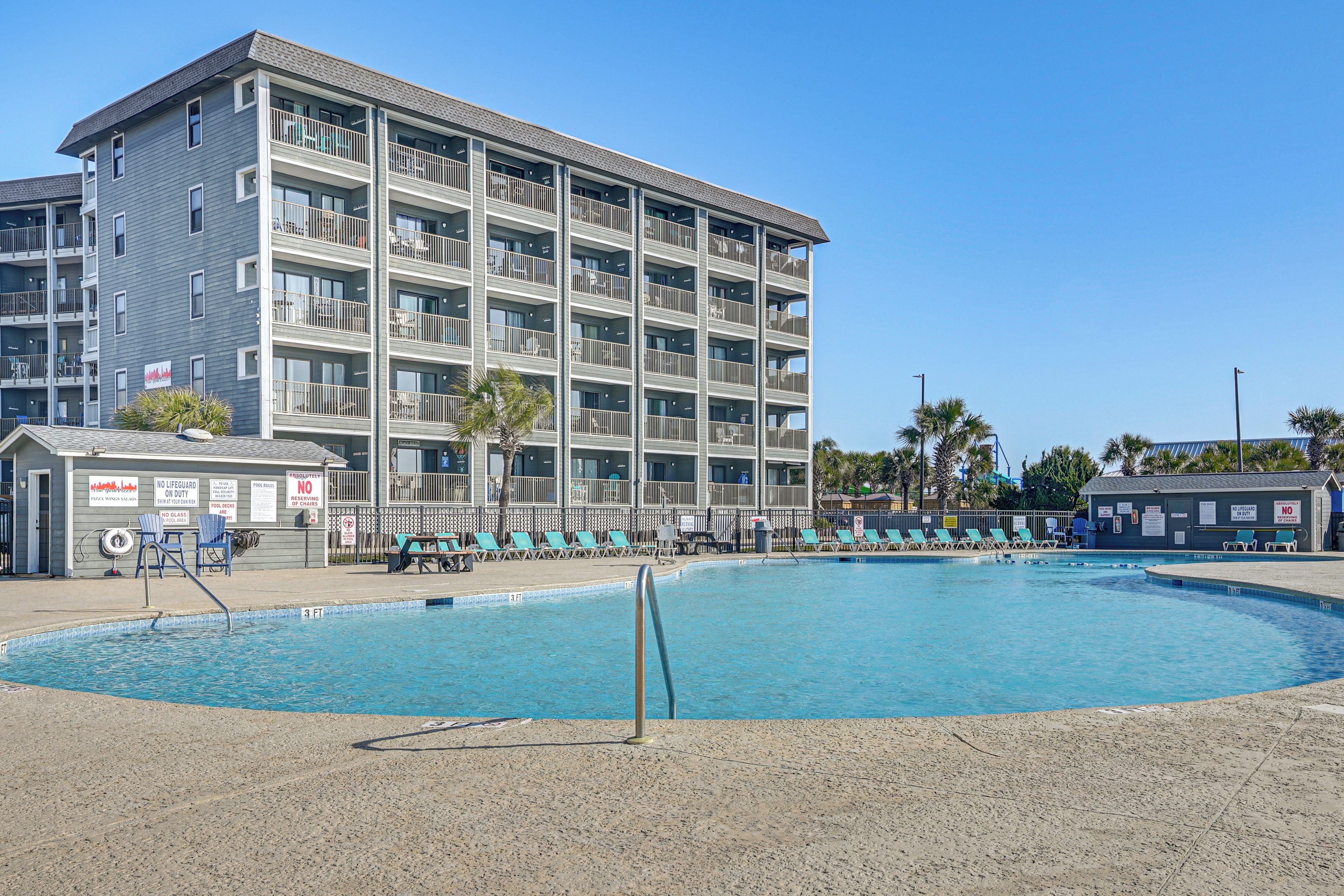 Un hôtel à plusieurs étages doté d’une piscine, de chaises longues et d’un poste de surveillance pour les sauveteurs.