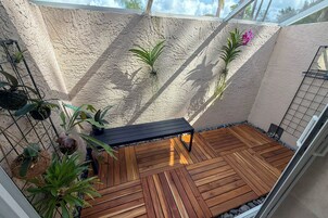 Una terraza de madera con un banco, rodeada de plantas en macetas y una pared con textura.