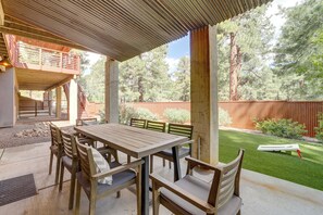 An outdoor patio with a wooden table and chairs, a covered seating area, and a fenced backyard with trees. - Near Trails, Skiing & Nau! Family-ready Home (Flagstaff)