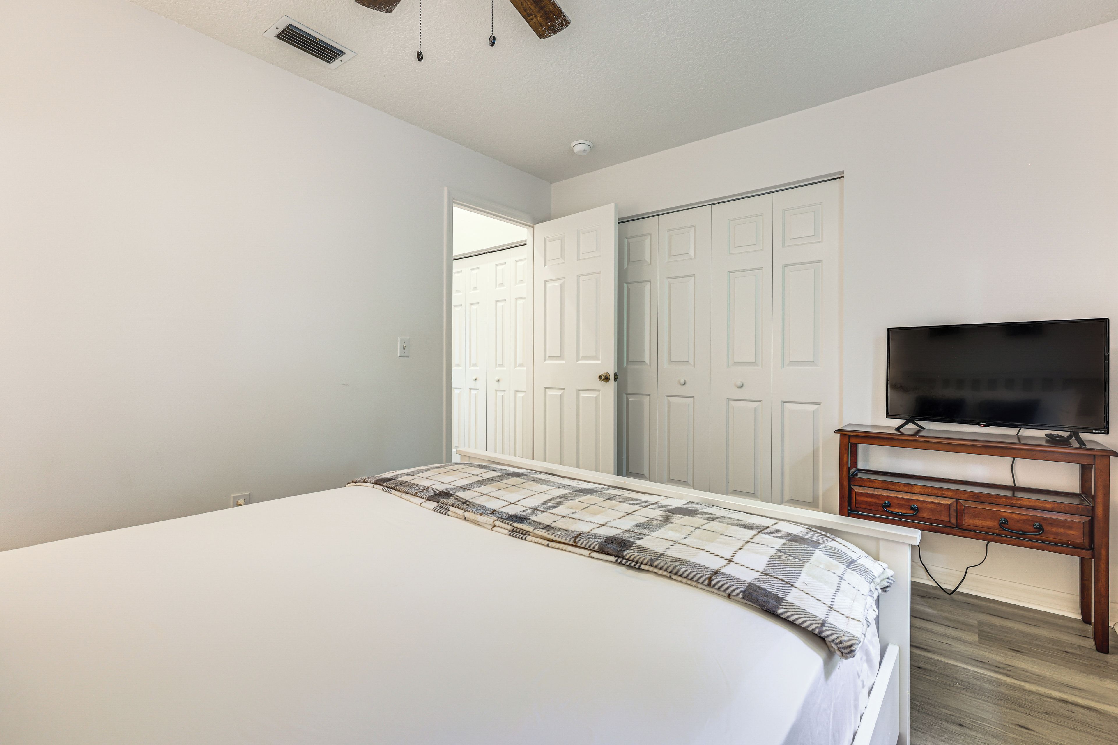 Quarto com cama, televisão sobre um suporte de madeira e guarda-roupa.