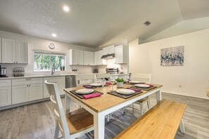 Una cocina moderna con armarios blancos, una mesa de comedor preparada para cuatro personas y vistas al exterior a través del ventanal.
