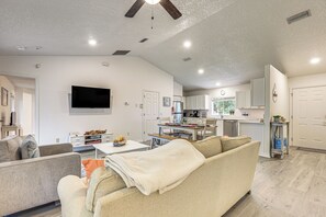 Sala de estar moderna com sofá, TV de tela plana e área de jantar com mesa posta para dois.