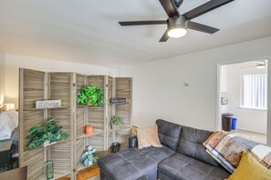 A living room with a sectional sofa, a ceiling fan, and a wooden partition with plants and signs. - Executive Oasis With In-suite Laundry Near Beach (Long Beach)