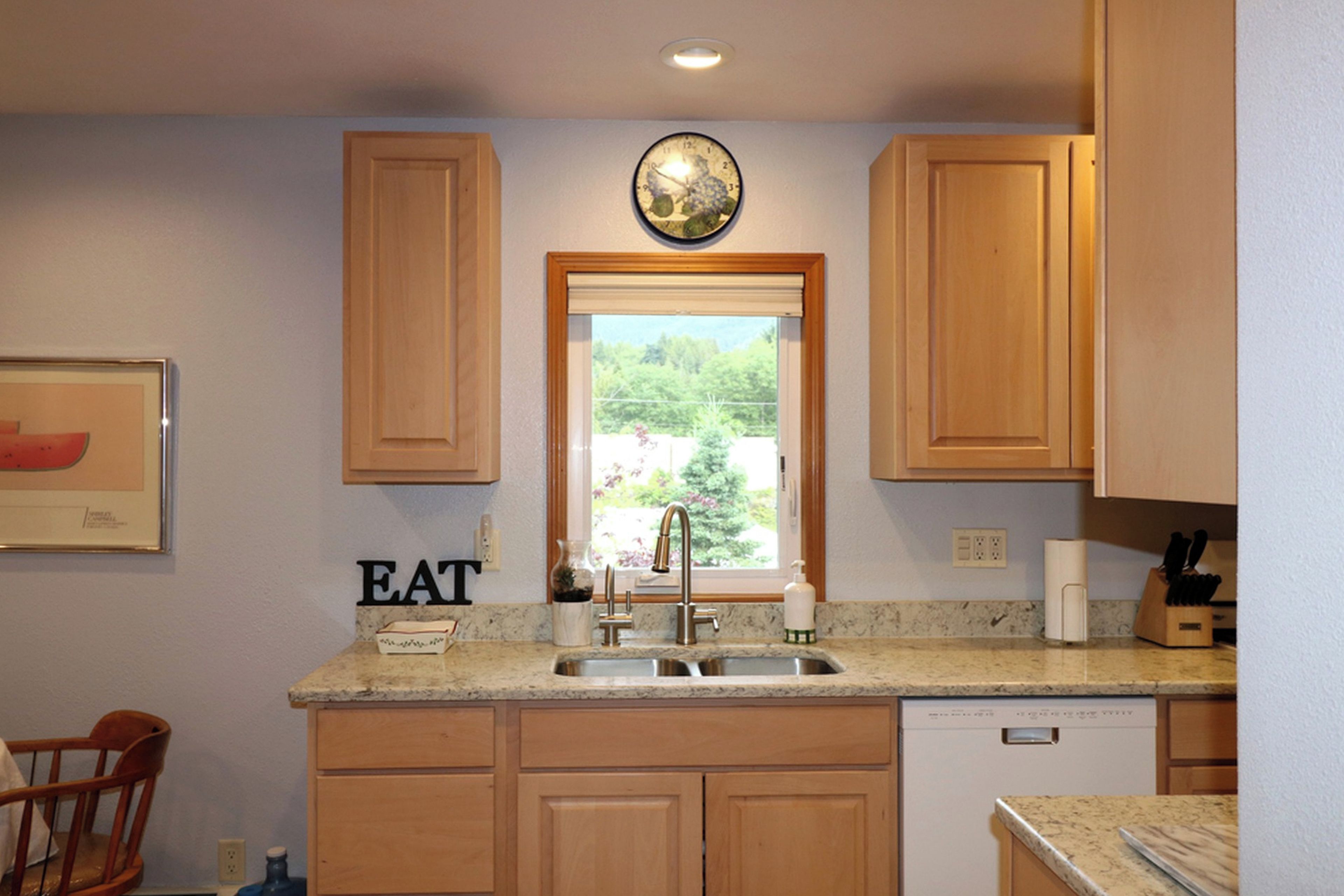 A kitchen with wooden cabinets, a built-in dishwasher, a sink with a faucet, and a window with a view of greenery.