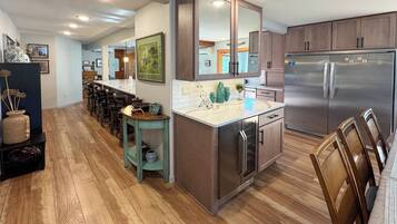 A modern kitchen with wooden cabinets, a stainless steel refrigerator, and a bar area with stools.