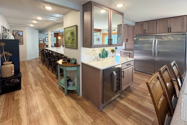 A modern kitchen with wooden cabinets, a stainless steel refrigerator, and a bar area with stools.