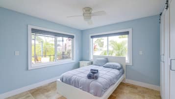 Quarto com cama, duas janelas, ventilador de teto e vista para o exterior.