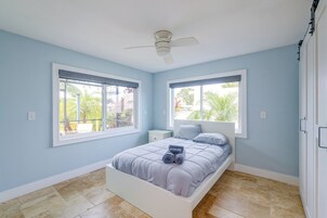 A bedroom with a bed, two windows, a ceiling fan, and a view of the outdoors.
