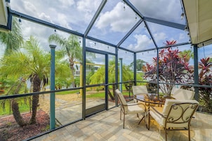 Un invernadero con techo de cristal, que cuenta con una zona de estar con sillas y una mesa, rodeado de plantas tropicales y vistas al exterior.