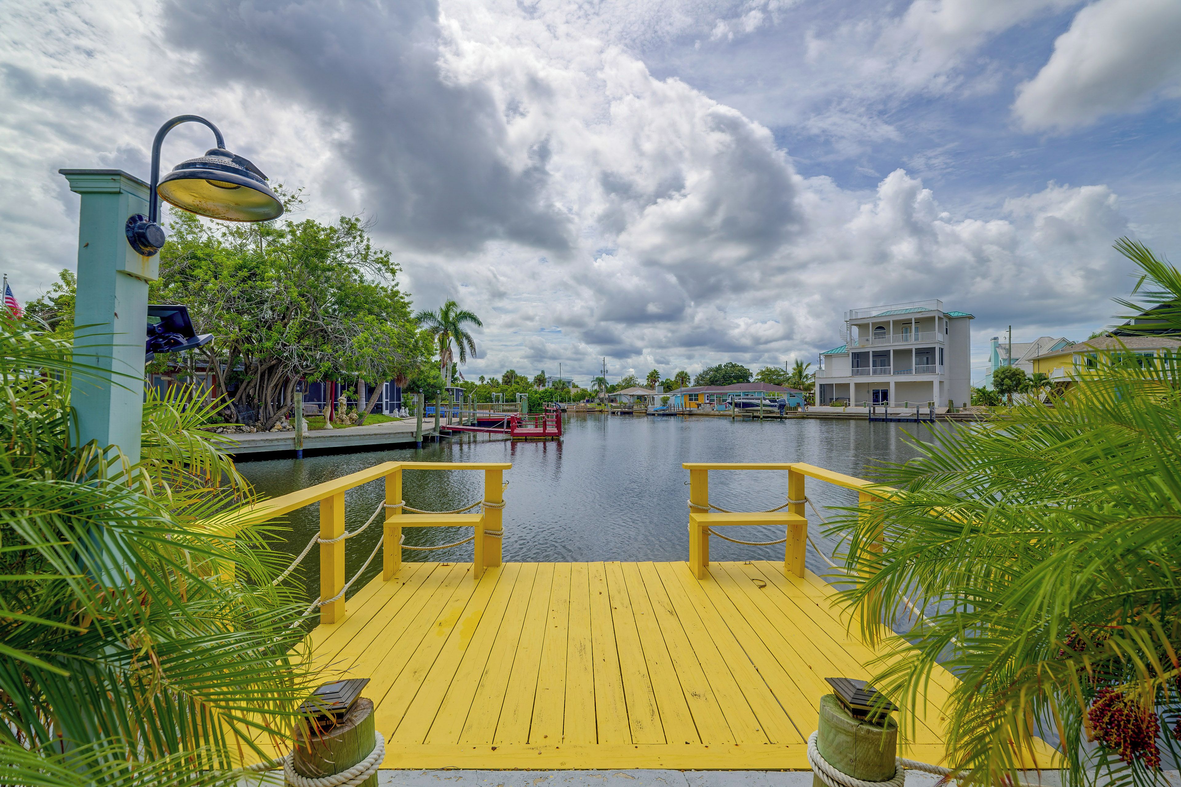 A waterfront dock with a yellow railing, a lamp post, and a view of a calm river with boats.