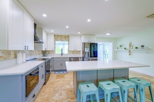 Una cocina moderna con armarios blancos, una isla central con taburetes y vistas al área de comedor.