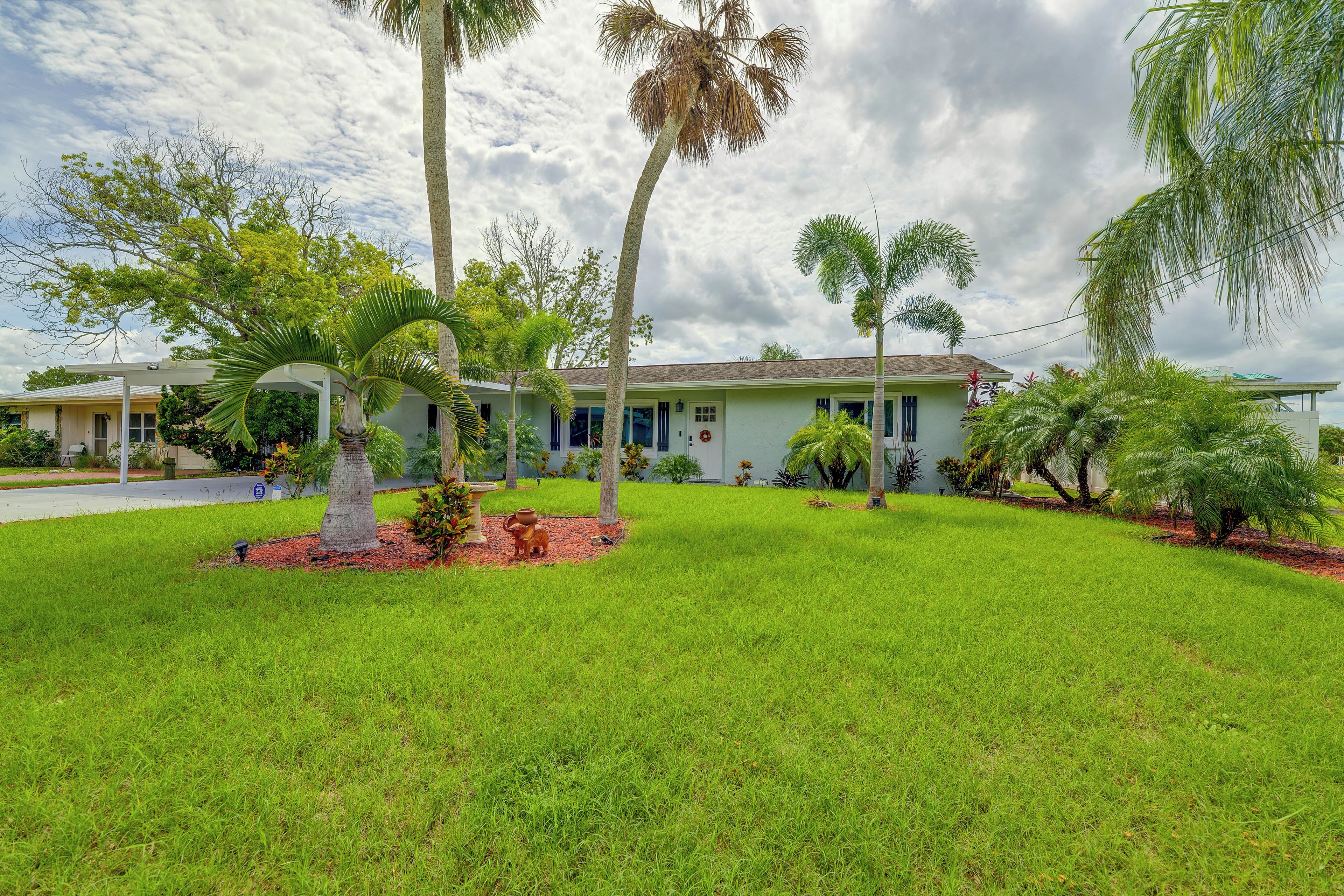 A residential property with a well-maintained lawn, palm trees, and a house with a green roof.