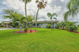 A residential property with a well-maintained lawn, palm trees, and a house with a green roof.