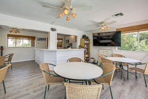 A spacious living area with a central island, wicker furniture, a flat-screen TV, and a large window offering a view of greenery. - Secluded Island Escape on Little Gasparilla Island (Placida)