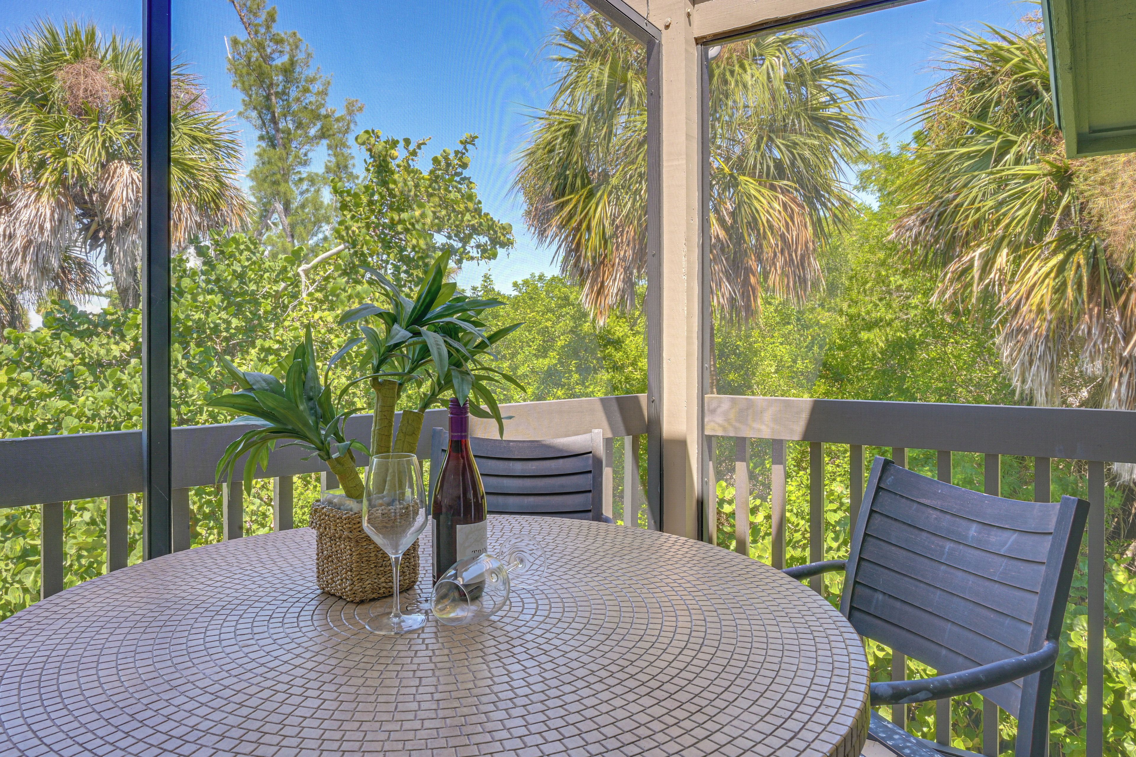 A round table with a woven basket, a bottle of wine, and a glass on a balcony with a view of palm trees.