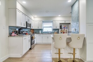 A modern kitchen with white cabinetry, stainless steel appliances, and a central island with bar stools. - Fully Remodeled Brandon Escape w/ Fenced Yard! (Brandon)