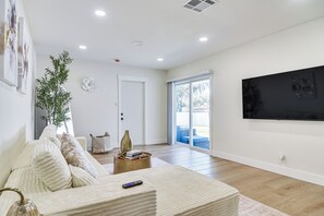 Ein Wohnzimmer mit einer Couch, einem Couchtisch, einer Pflanze und einem Fernseher an der Wand.