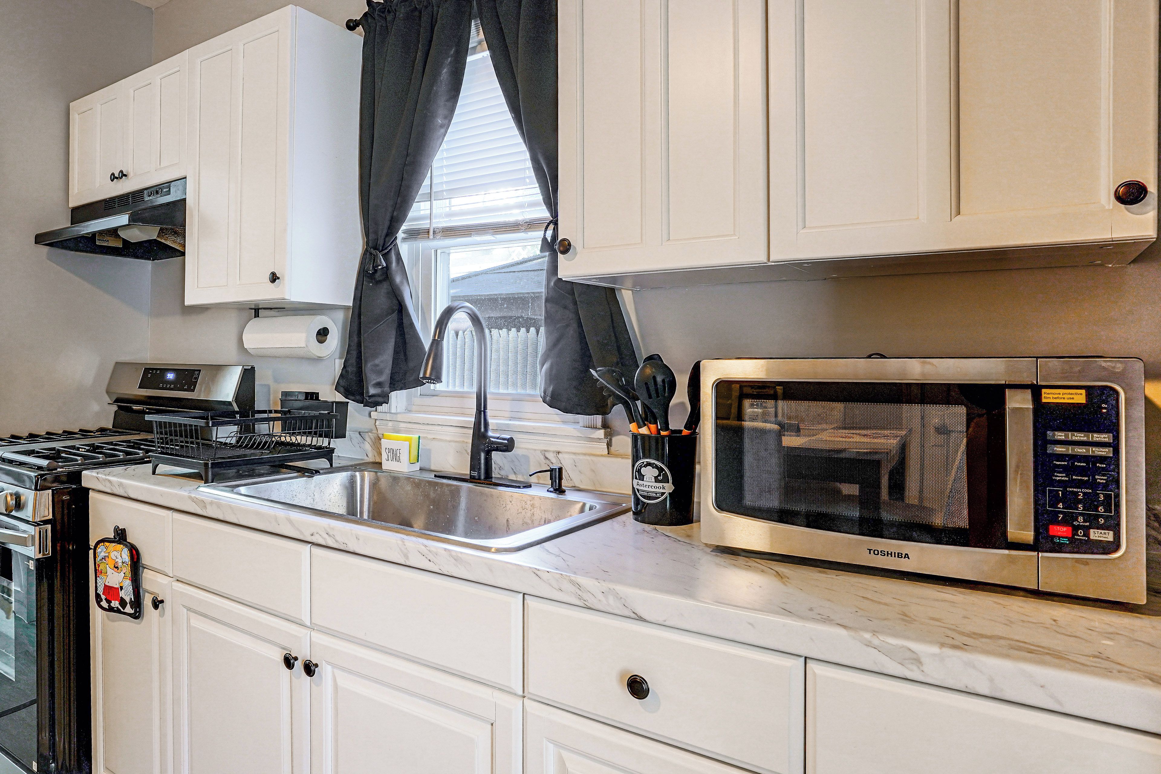 A kitchen with white cabinets, a stainless steel sink, a stove, and a microwave.