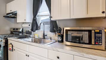 A kitchen with white cabinets, a stainless steel sink, a stove, and a microwave.