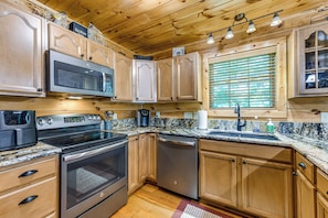 A kitchen with wooden cabinets, stainless steel appliances, a granite countertop, and a window with blinds. - 5 Mi to Cataloochee Ski! Mtn-view Retreat w/ Deck (Maggie Valley)