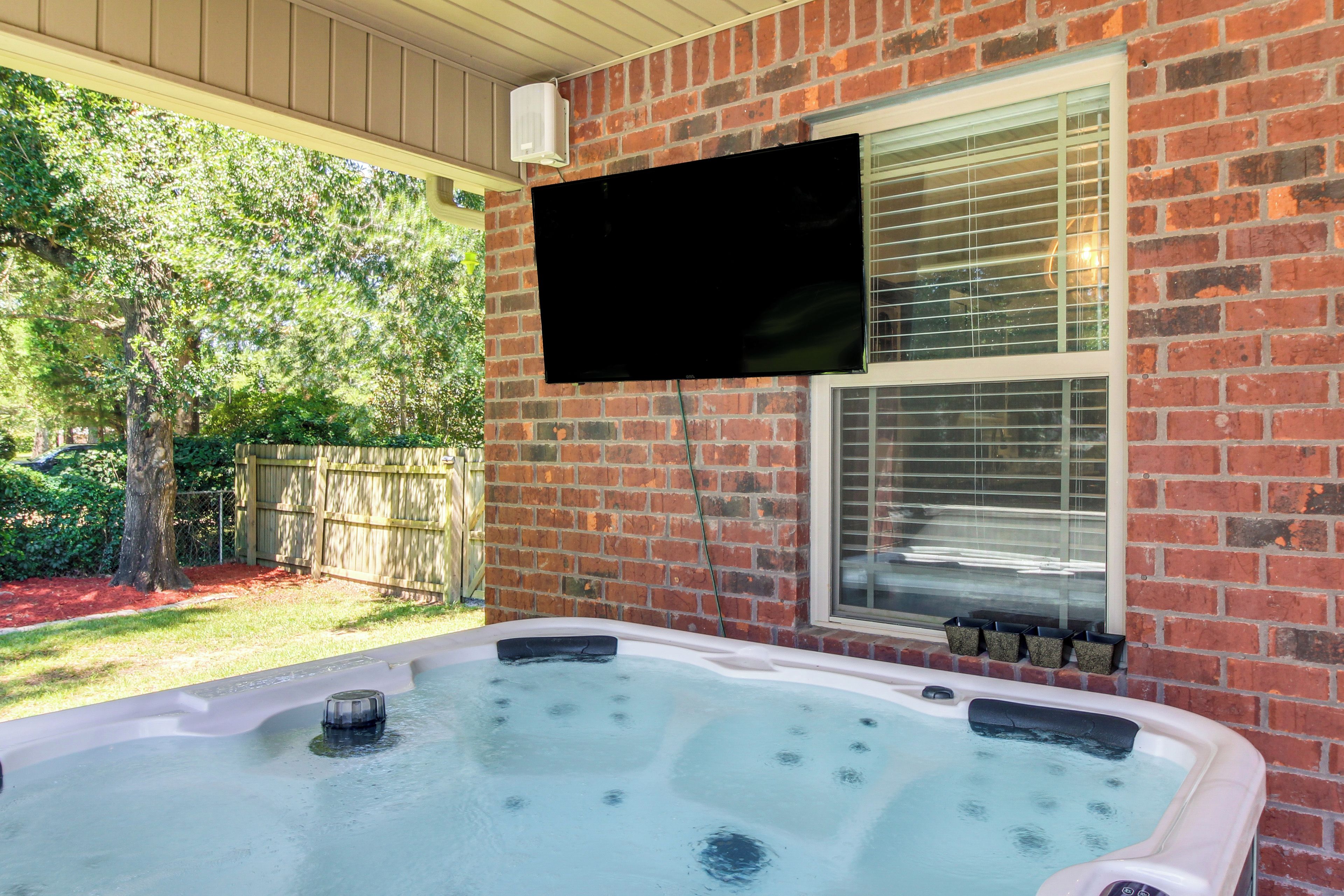 A hot tub with jets, a television mounted on the wall, and a brick exterior.
