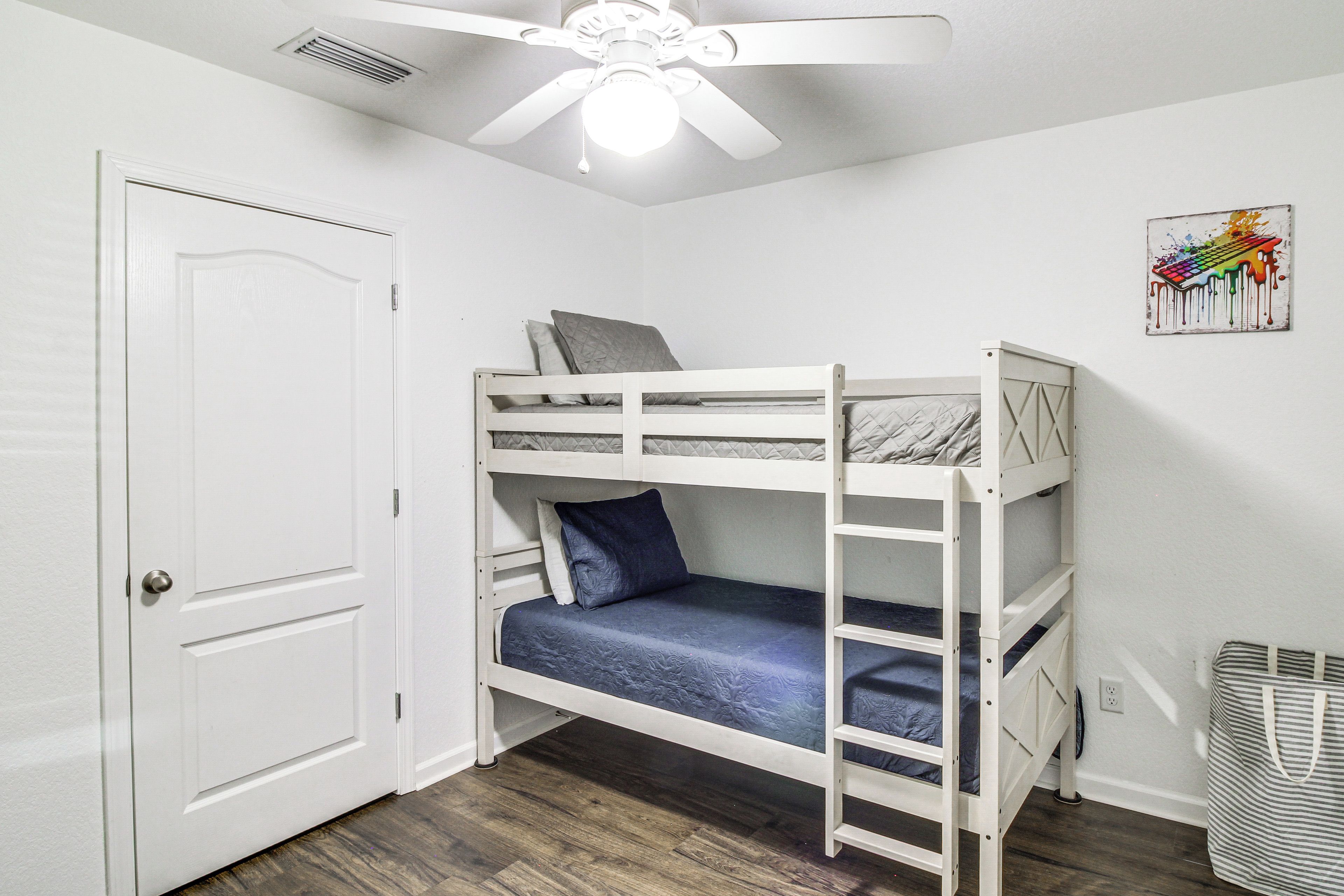 A bunk bed room with a ceiling fan, a door, and a wall-mounted artwork.