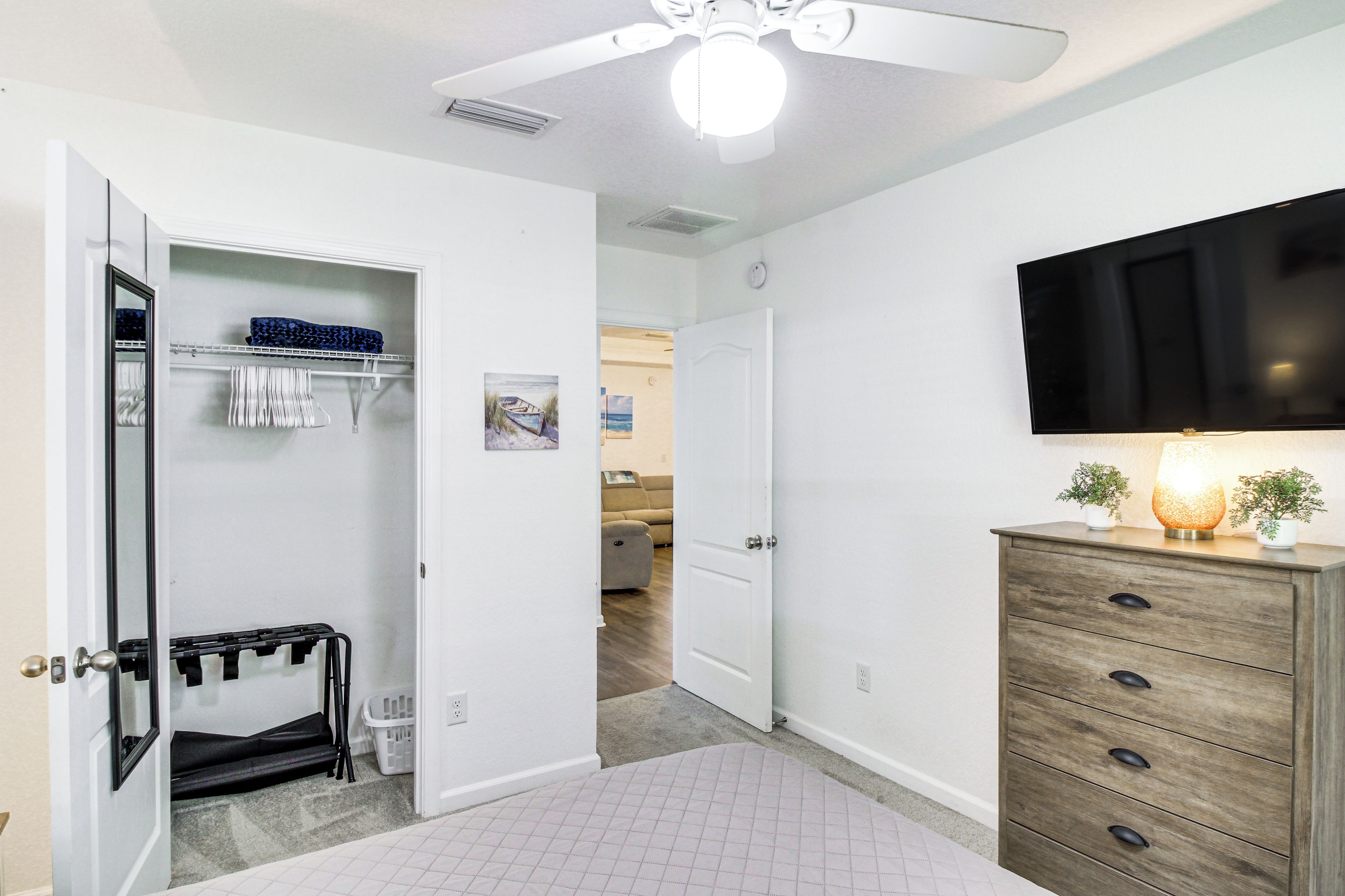 A hotel room with a closet, a wooden dresser, a flat-screen TV, and a ceiling fan.