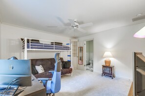 Una habitación con literas, un escritorio con computadora, una silla, una lámpara y un ventilador de techo.
