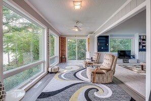 Una sala de estar amplia con ventanas grandes, chimenea, ventilador de techo y televisor.