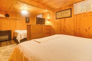 Un dormitorio de cabaña de madera con una cama, un tocador, un televisor y una mesita.
