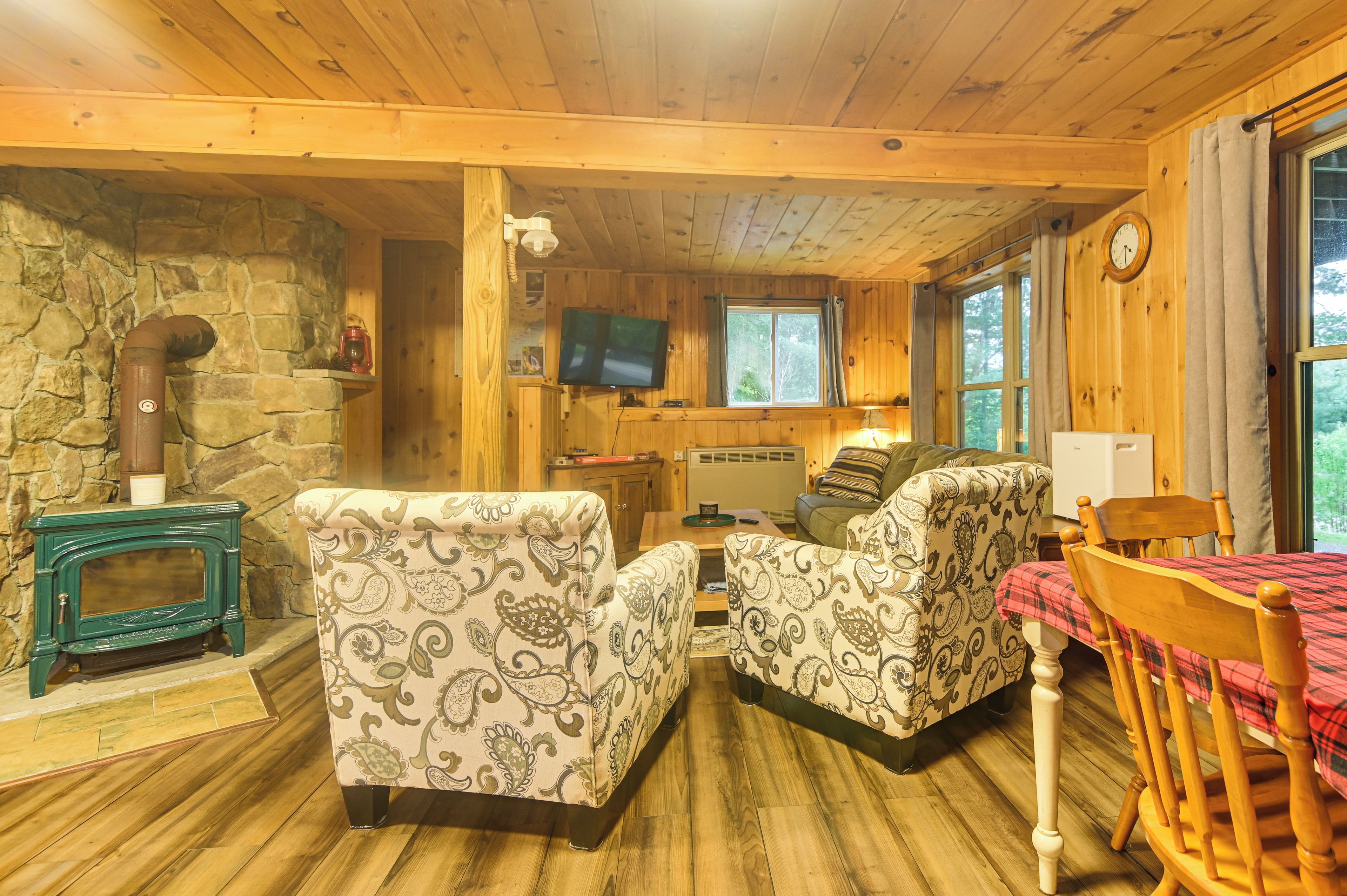 Un interior de cabaña acogedor con chimenea de piedra, paredes de madera, un televisor y un comedor.
