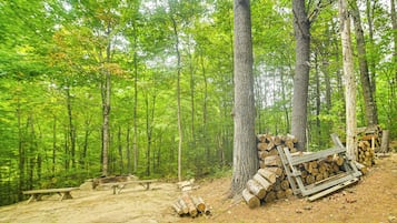 Un campeggio immerso nel verde con tavoli da picnic e una pila di legna da ardere.
