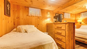 En stuga med trÀpanel, inredd med tvÄ sÀngar, en byrÄ, en tv och en vÀggklocka.