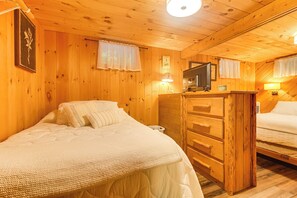 A wooden cabin room with two beds, a dresser, a television, and a clock on the wall.