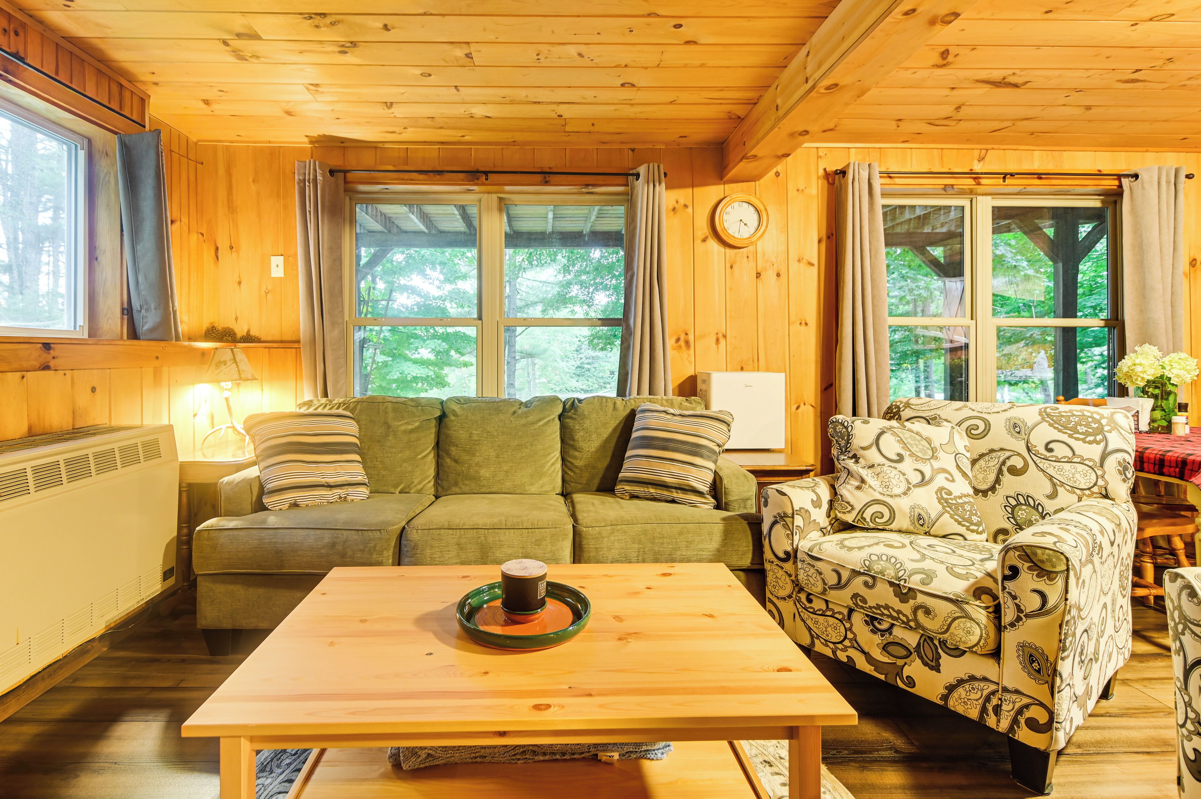 A cozy cabin interior with a sofa, patterned armchair, and a table with a mug.