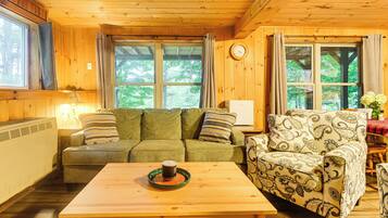 A cozy cabin interior with a sofa, patterned armchair, and a table with a mug.