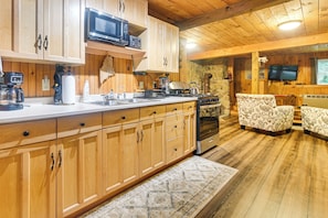 A kitchen with wooden cabinets, a microwave, a stove, and a sink. There is a patterned rug on the floor.