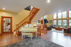 A spacious living room with a grand piano, a wooden staircase, and large windows. - Spacious Executive Home on Over 11 Private Acres (Rockford)