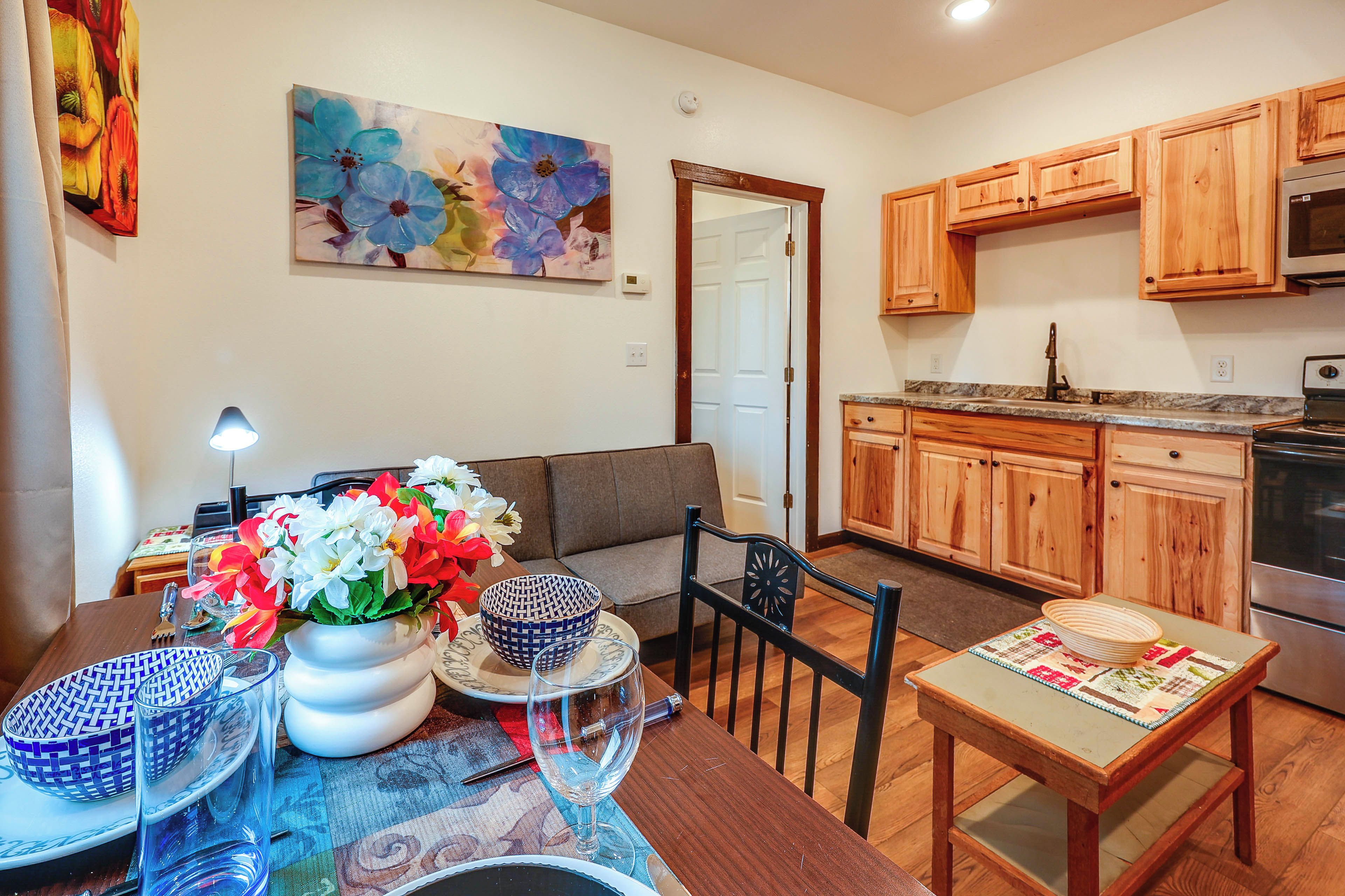 A modern kitchen with wooden cabinets, a dining area with a table set for two, and a sofa.