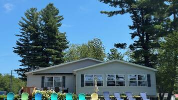 A single-story mobile home with a front porch, surrounded by a grassy lawn and trees.