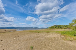 A natural landscape with a beach, a body of water, and distant mountains under a partly cloudy sky.