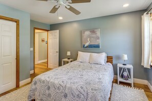 A bedroom with a bed, two bedside tables, a ceiling fan, a painting, and a view of a hallway. - Lakefront Adirondack Escape! Fire Pit & Game Room (Broadalbin)