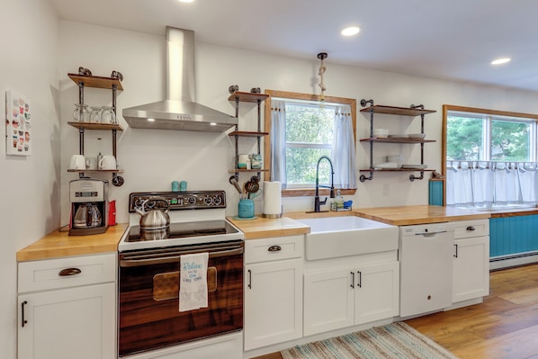 A modern kitchen with white cabinetry, a stainless steel range hood, and wooden countertops.