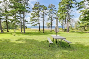 A picnic table with a canopy in a grassy area with trees and a view of a body of water.