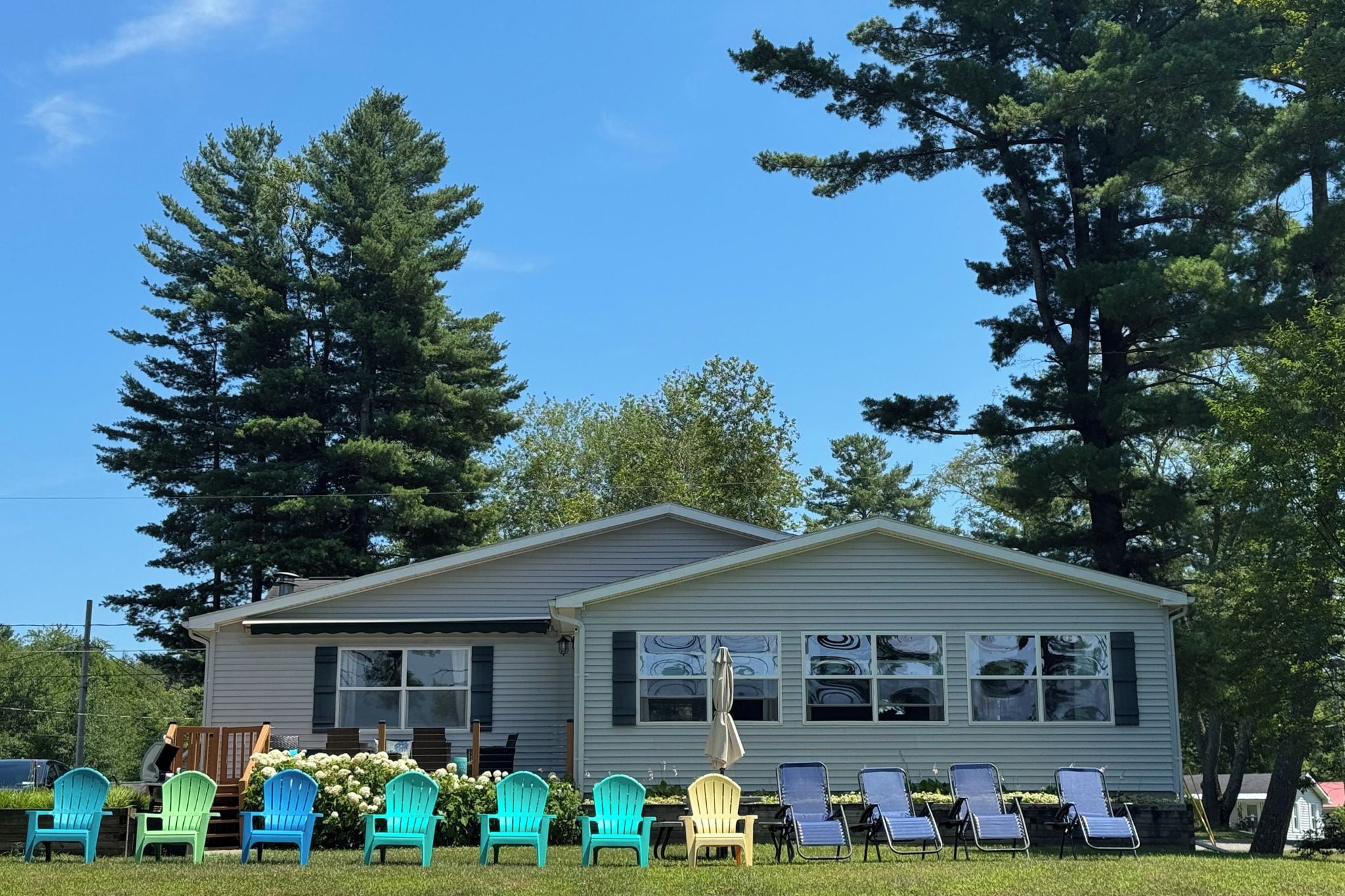 A single-story mobile home with a front porch, surrounded by a grassy lawn and trees.