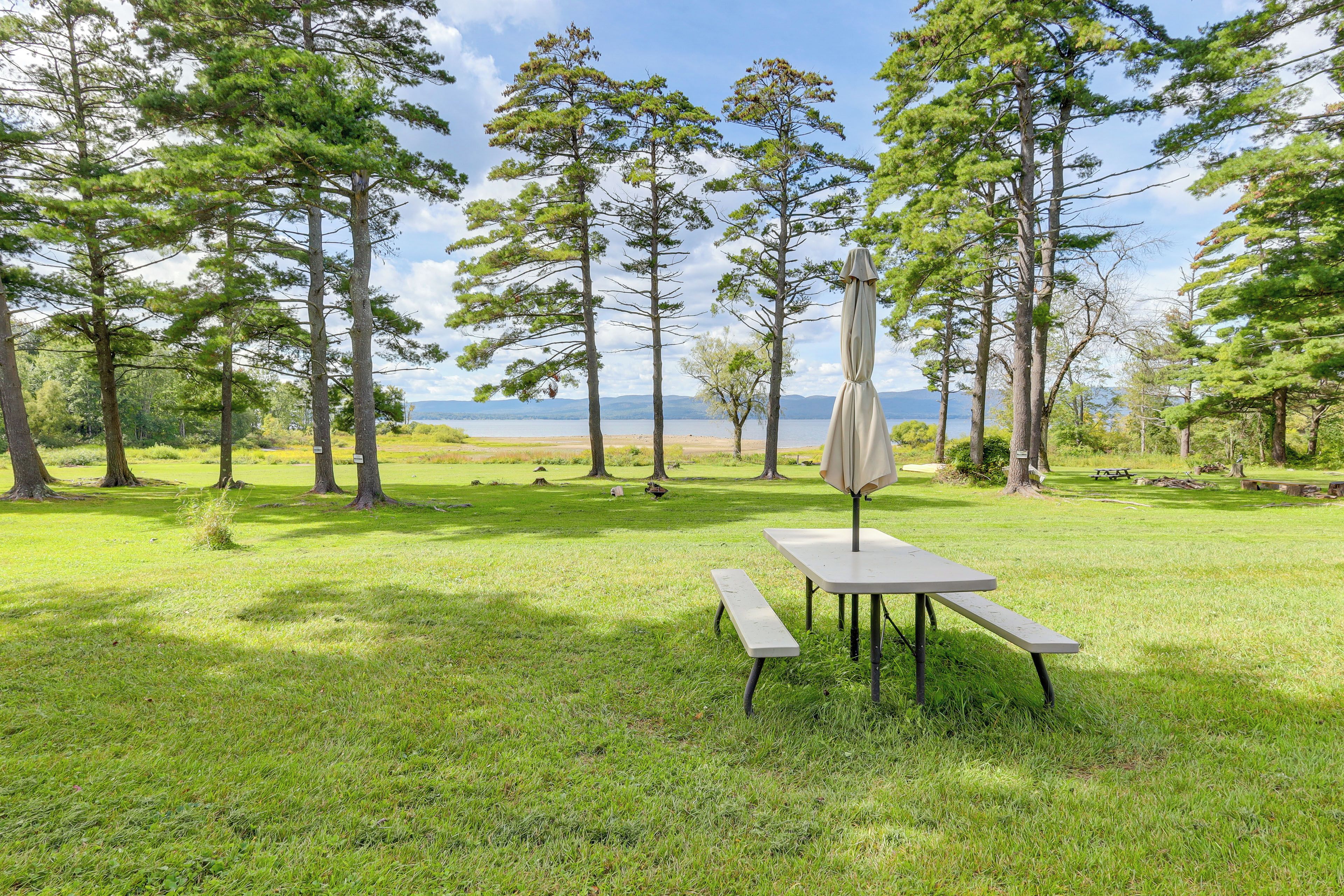 A picnic table with a canopy in a grassy area with trees and a view of a body of water.